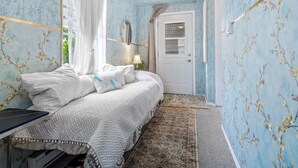 A bedroom with a bed, a desk, a door, and a window with curtains.