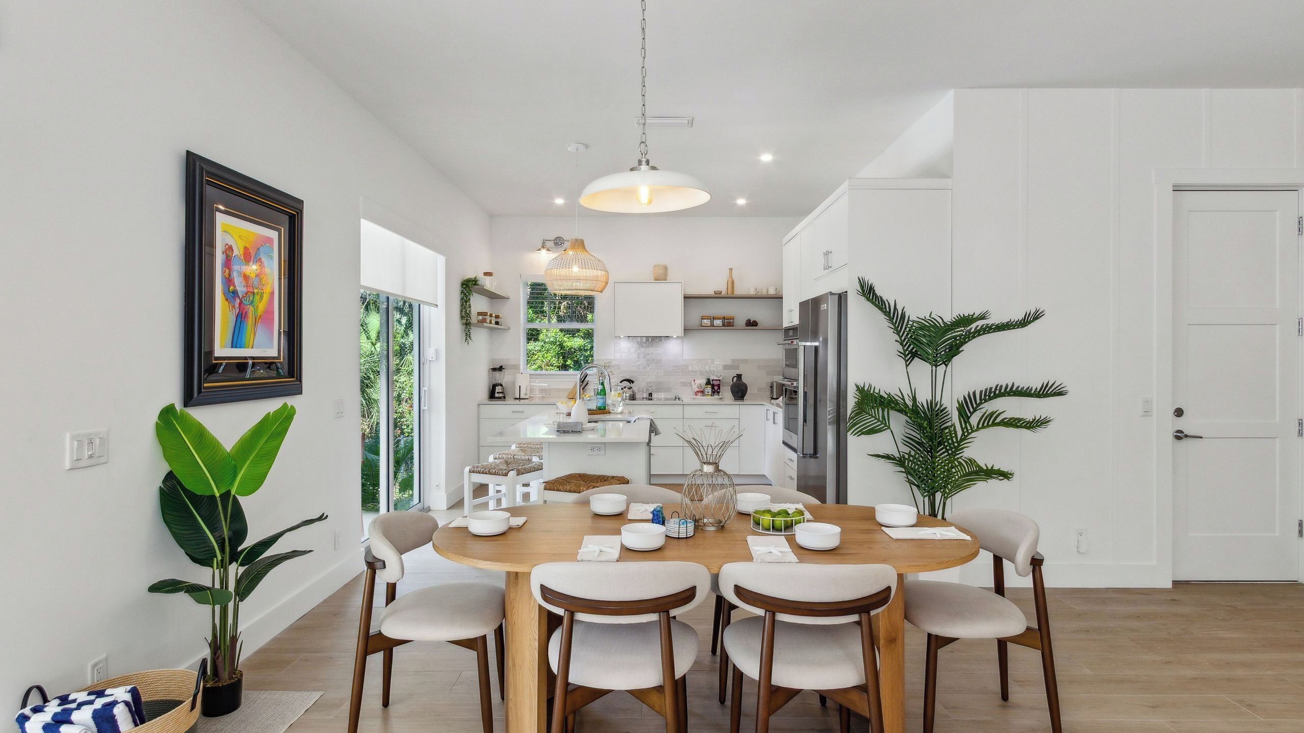 Una cucina moderna con mobili bianchi, un frigorifero in acciaio inossidabile e un'area pranzo con tavolo e sedie in legno.