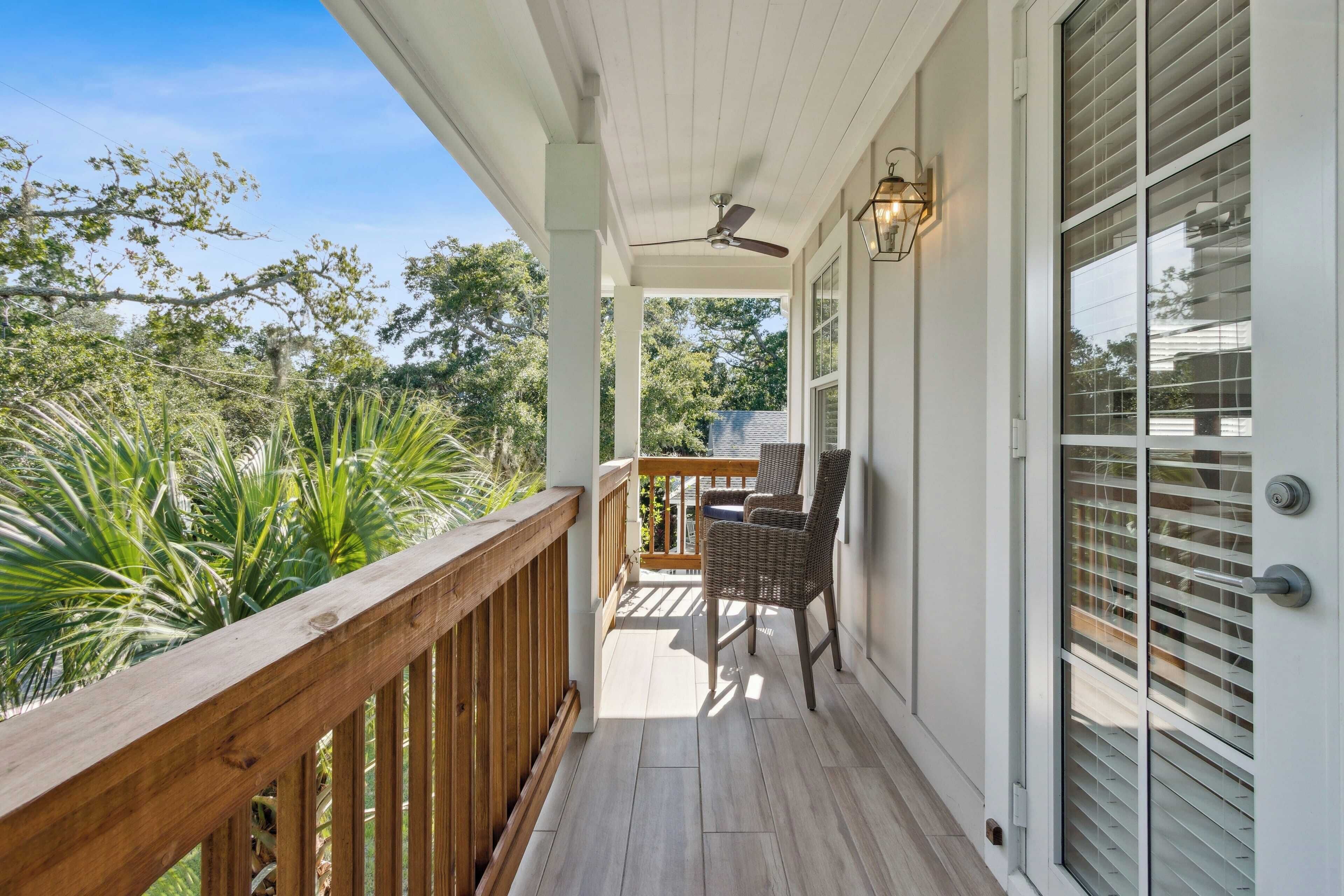 A covered porch with a wooden railing, wicker chairs, and a ceiling fan.