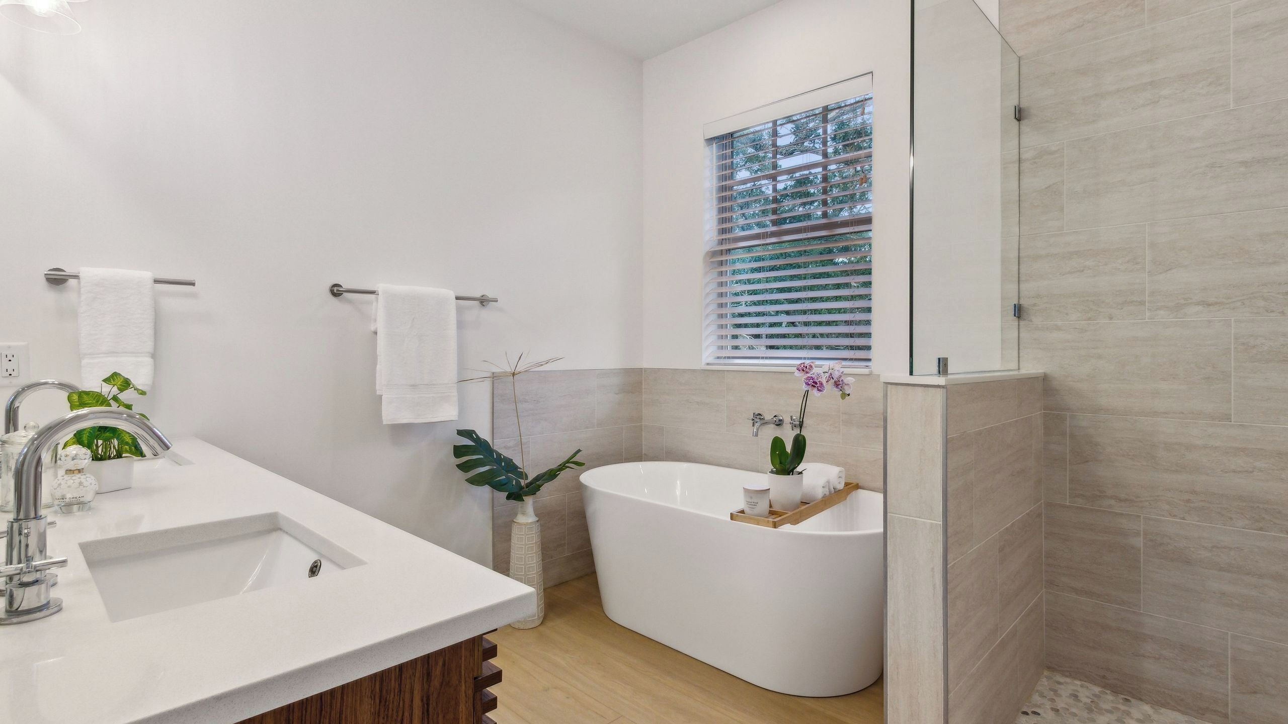 A modern bathroom with a freestanding bathtub, a vanity with a sink, and a window with blinds.