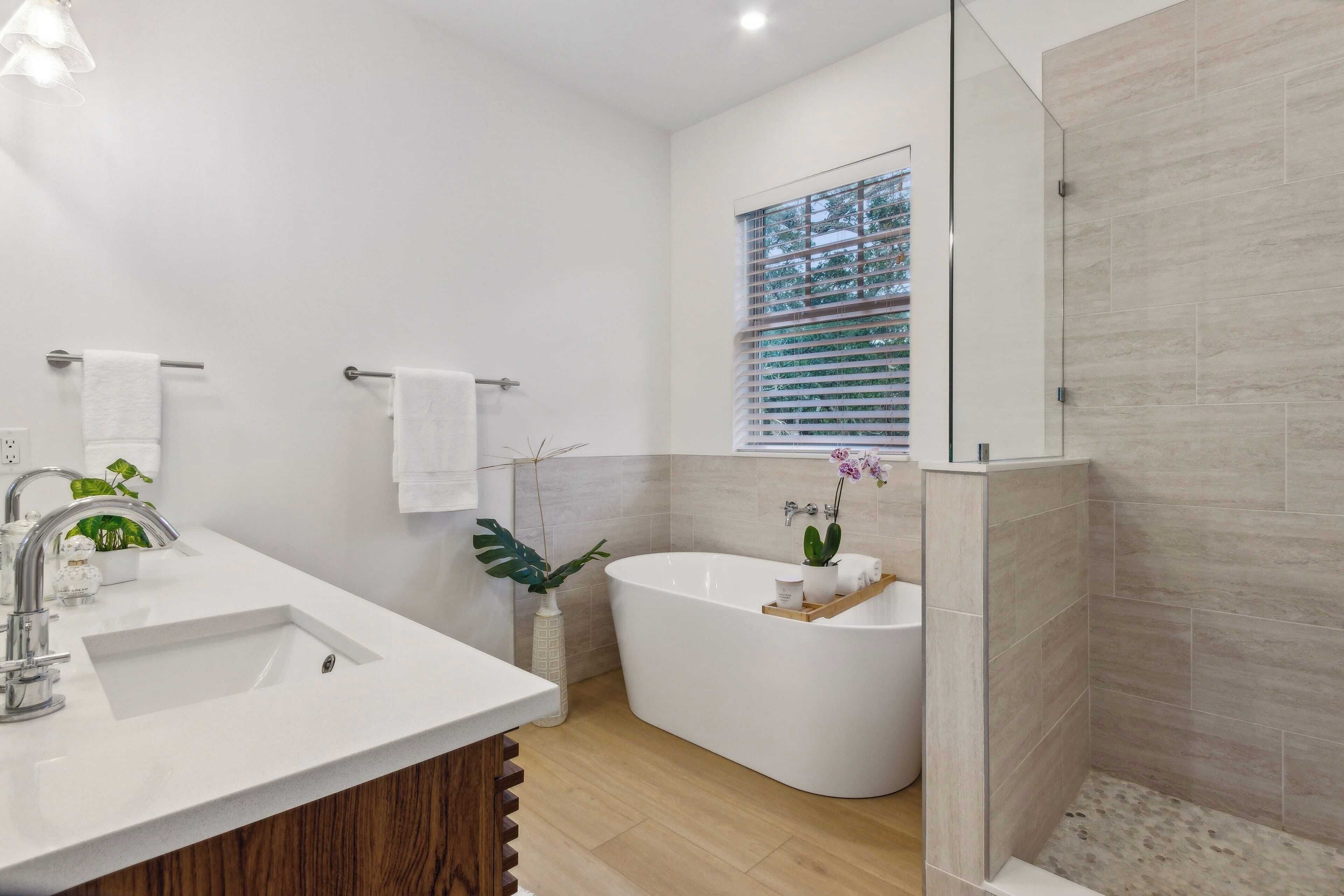 A modern bathroom with a freestanding bathtub, a sink with a mirror, and a window with blinds.