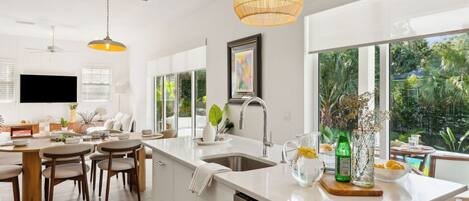 A modern kitchen with a large island, a dining area, and a view of greenery.