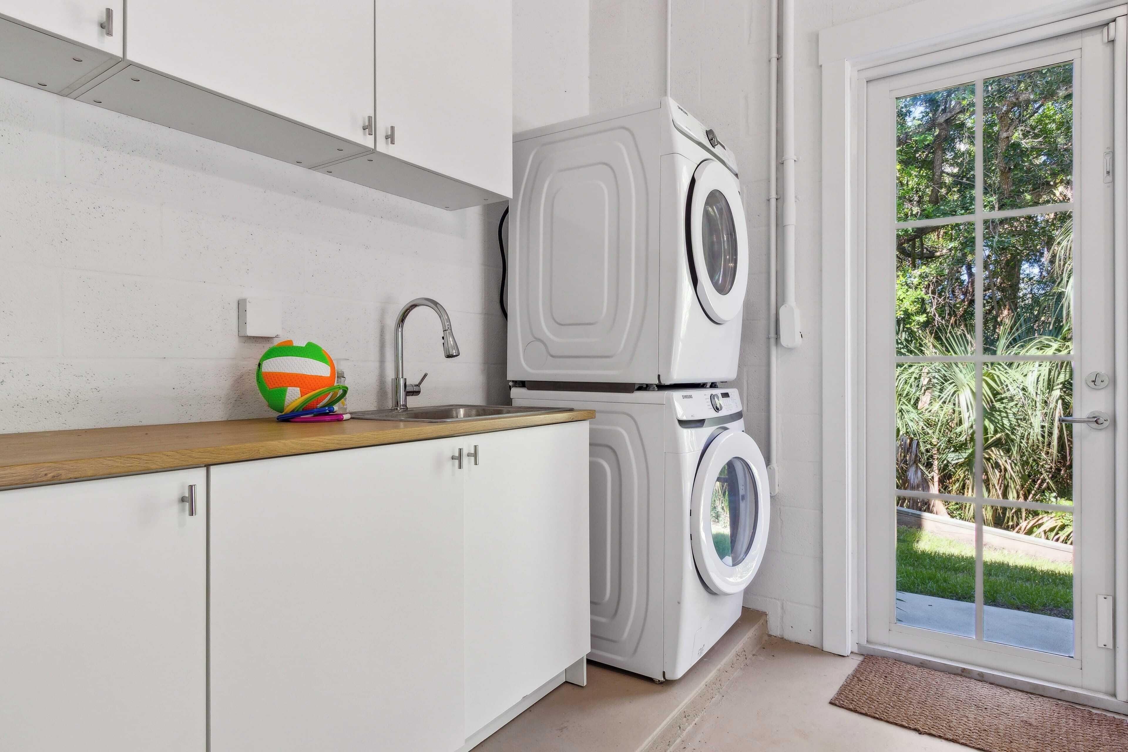 A laundry area with a washing machine and dryer, a sink, and a view of the outdoors through a glass door.