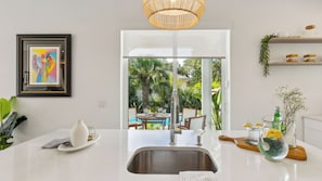 A modern kitchen with a large sink, dining area, and a view of a tropical garden.