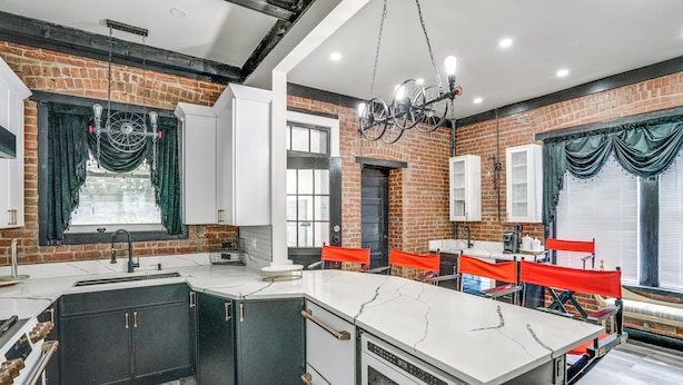 A modern kitchen with a large island, black and white cabinetry, and a brick accent wall. - Steps to Union College: Home w/ Shared Yard! (Schenectady)