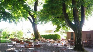 Un espace extérieur aménagé pour les repas, avec des tables et des chaises disposées sous de grands arbres.