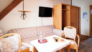 Une pièce chaleureuse avec un plafond en bois, un canapé, une table avec une télécommande et un téléviseur fixé au mur.