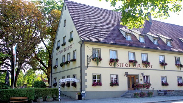 Un bâtiment traditionnel avec une enseigne indiquant « Gasthof Zur Post » et « Biergarten », ce qui signifie qu’il s’agit d’un restaurant avec un jardin à bière.