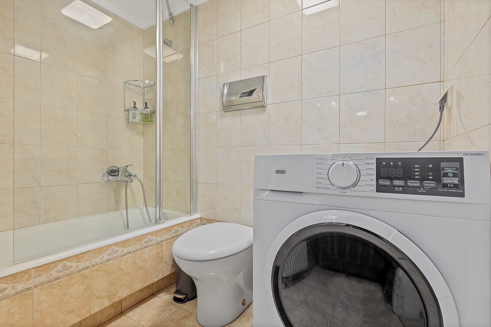 A bathroom with a glass shower enclosure, a toilet, and a front-loading washing machine.