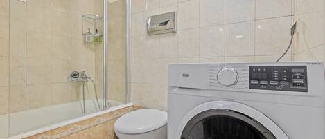 A bathroom with a glass shower enclosure, a toilet, and a front-loading washing machine.