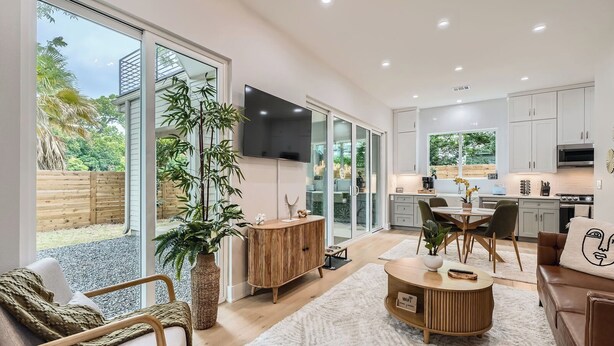 A spacious living area with a large sliding glass door leading to a backyard, a kitchen with modern appliances, and a cozy seating area with a flat-screen TV.