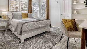 Une chambre à coucher comprenant un lit, des tables de chevet, une chaise, un bureau et un tapis à motifs.