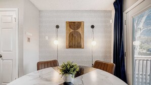 Un coin repas comprenant une table en marbre, deux chaises, une plante en pot et un mur décoré d’un motif original.