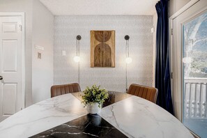 A dining area with a marble table, two chairs, a potted plant, and a patterned wall with a unique design.
