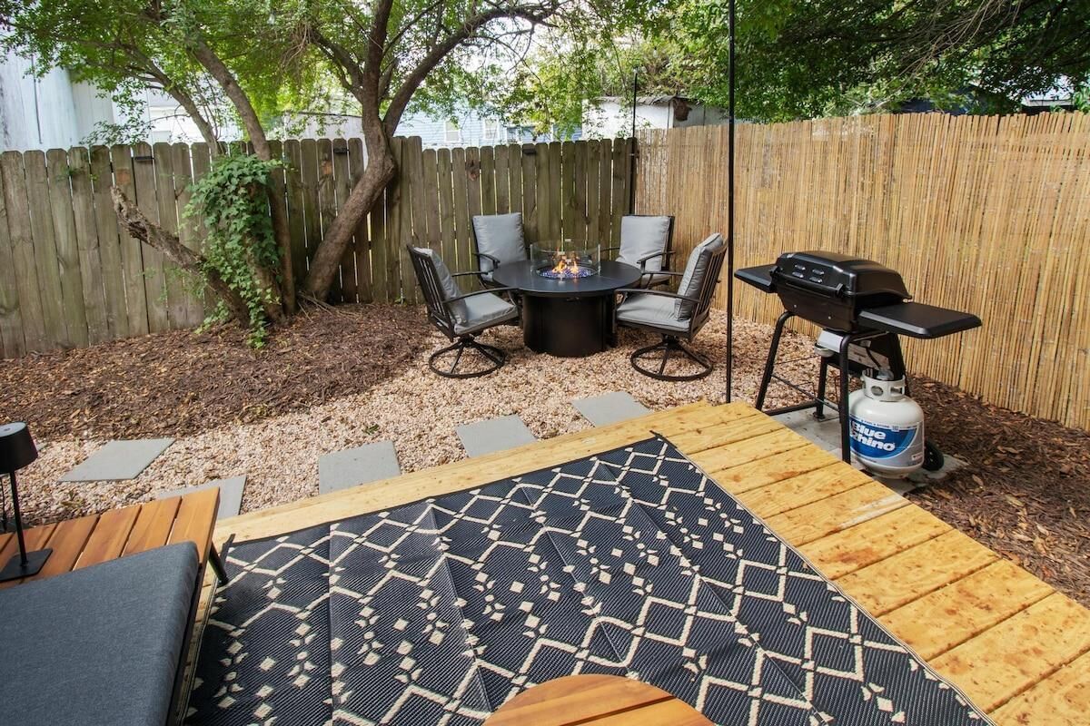 Un patio trasero con una mesa redonda y sillas, una parrilla de barbacoa y un área de estar cubierta.