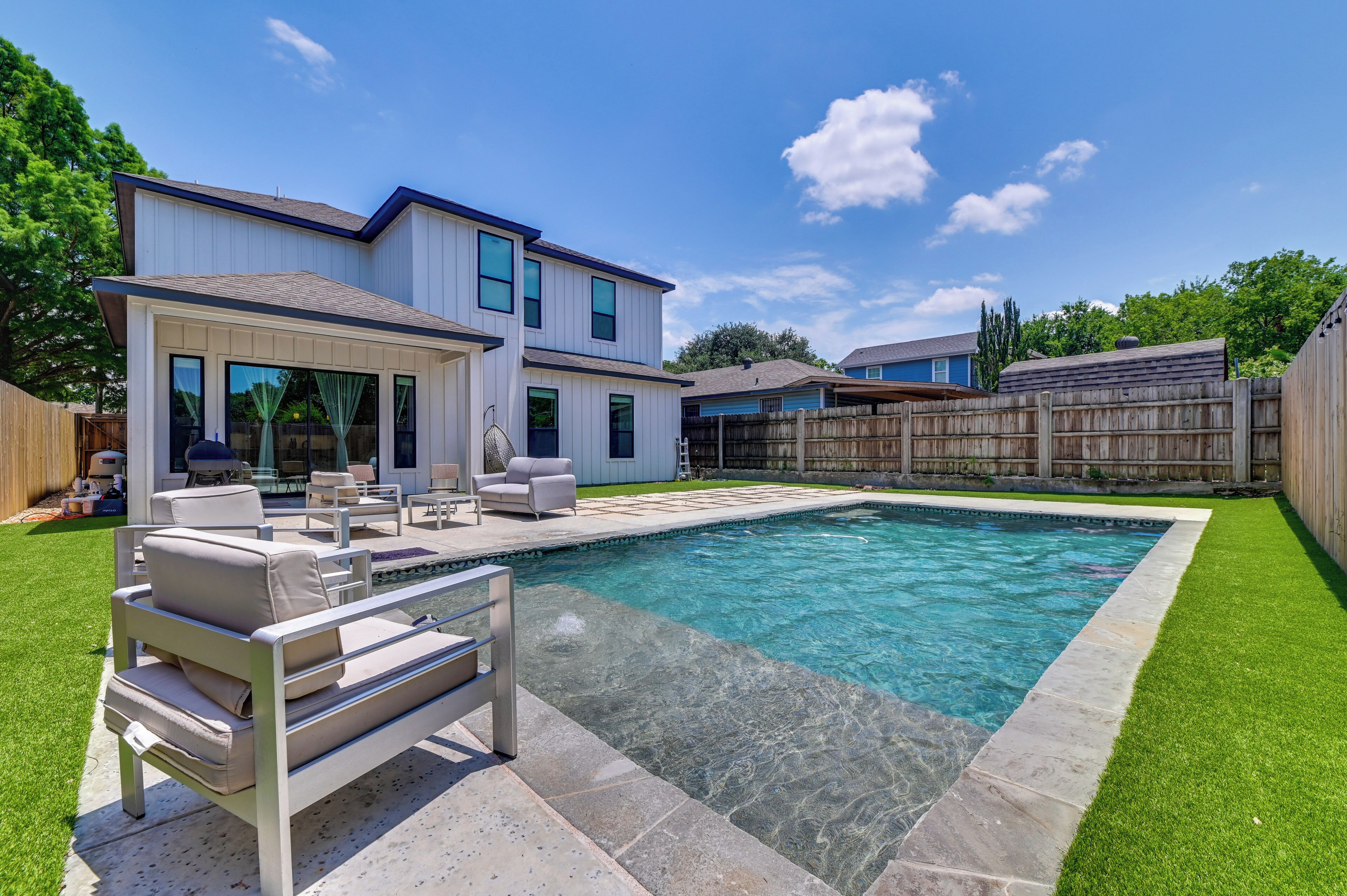 A modern two-story house with a swimming pool, outdoor seating, and a wooden fence.