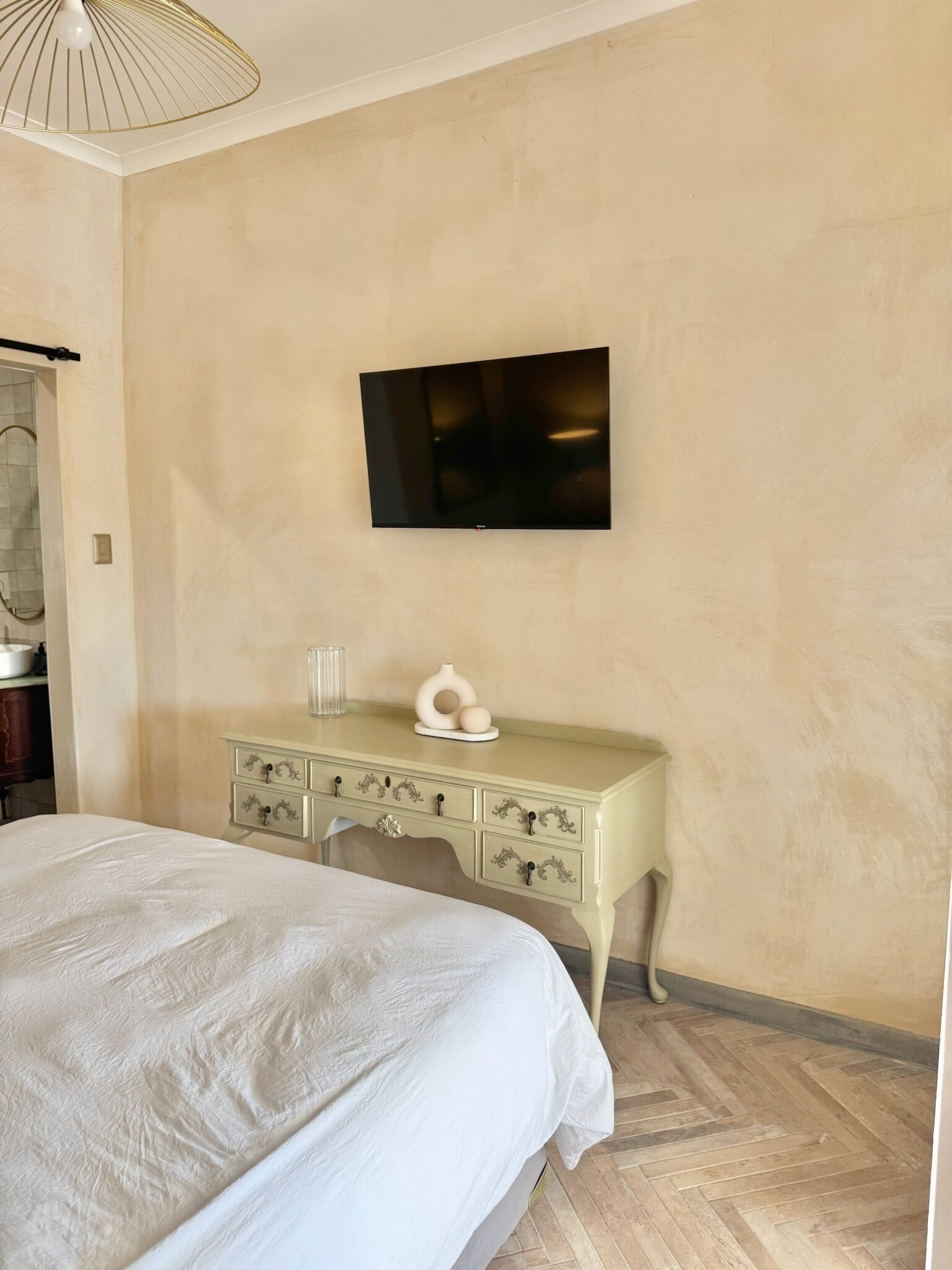 A bedroom with a bed, a dresser, a television on the wall, and a mirror.