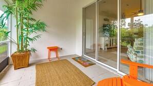 A balcony with a large potted plant, a small orange stool, and a woven mat. - Screened Lanai + Workspace! Naples Stay Near Gulf (Naples)