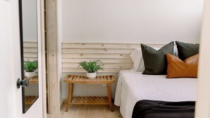 Ein Schlafzimmer mit schrägem Dach, einer Holzbank mit Topfpflanzen, einem Bett mit Kissen und einer Tür mit Spiegel.