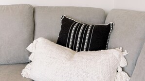 Ein graues Sofa mit einem weiß-schwarz gestreiften Kissen und einer weißen Strickdecke.