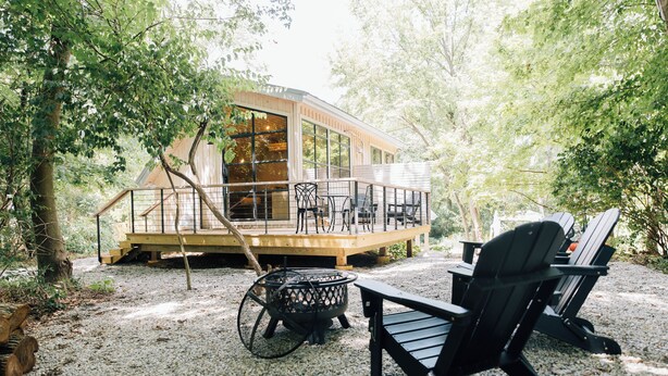 Eine Holzterrasse mit Sitzgelegenheiten im Freien und einem Feuerkorb, umgeben von Bäumen.