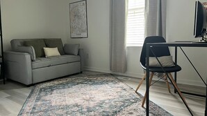 Un salon moderne avec un canapé gris, un fauteuil noir, un bureau et un tapis à motifs.