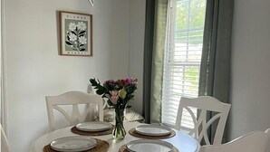 Une table de salle à manger ronde, entourée de chaises blanches, un vase rempli de fleurs et un tableau encadré accroché au mur.
