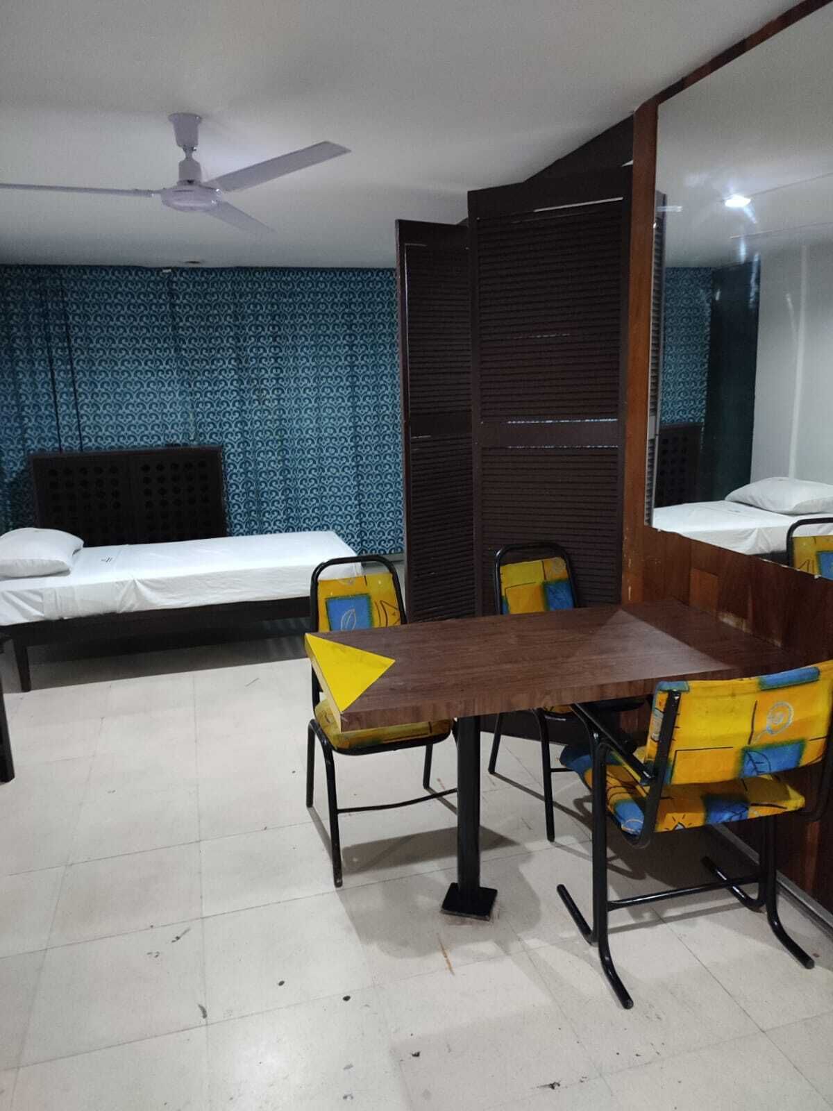 A room with a bed, a dining table with chairs, a ceiling fan, and patterned wallpaper.