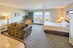 A hotel room with a bed, a sofa, a desk, a television, and a view of the beach.