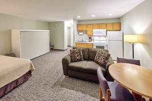 Une chambre d’hôtel compacte comprenant un coin cuisine, un canapé agrémenté de coussins à motifs, une petite table à manger et une chaise.