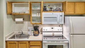 Una cucina compatta con forno a microonde, forno e frigorifero integrati. C'è una macchina da caffè e un lavello con porta asciugamani.