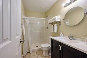 A bathroom with a shower, toilet, sink, and a mirror.