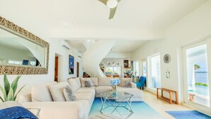 Un salon spacieux, doté d’un grand canapé d’angle, d’une table basse en verre et offrant une vue sur l’océan grâce à de grandes fenêtres.