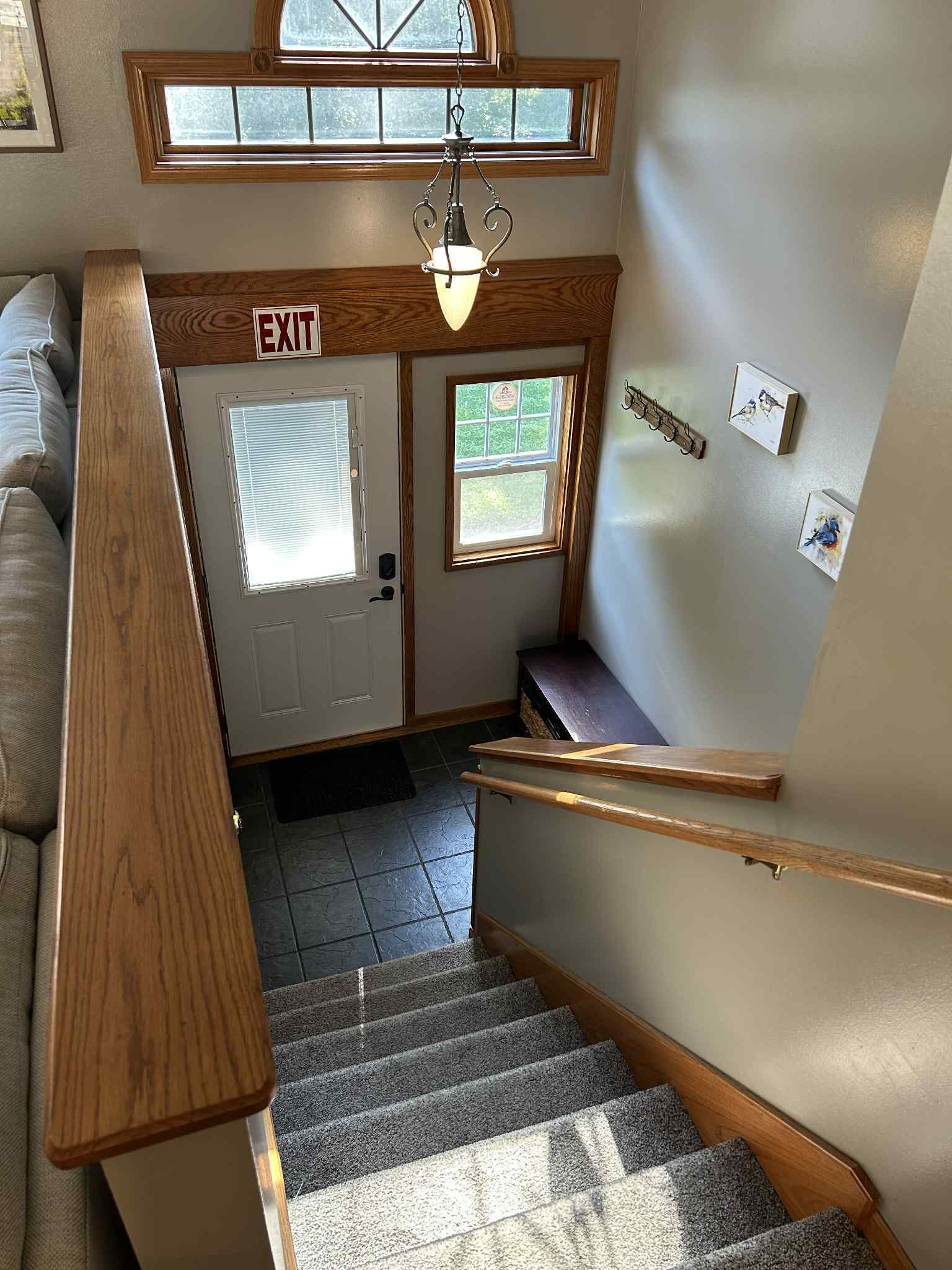 A staircase with wooden handrails, a bench, and an exit sign.