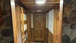 Un pasillo de madera con un muro de piedra, una puerta de madera y una alfombra en el suelo.