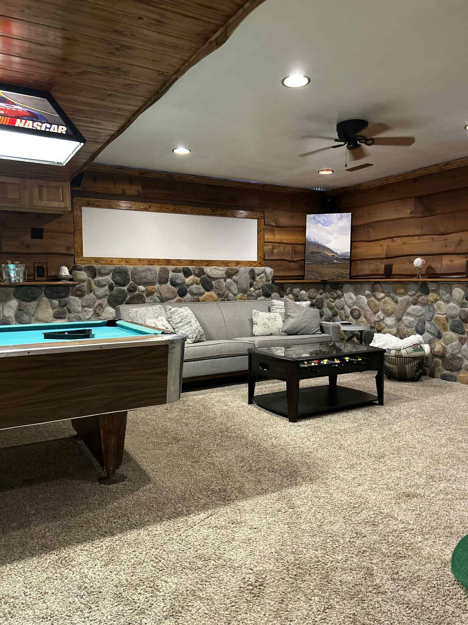 A cozy indoor space with a pool table, a sofa, and a stone wall.