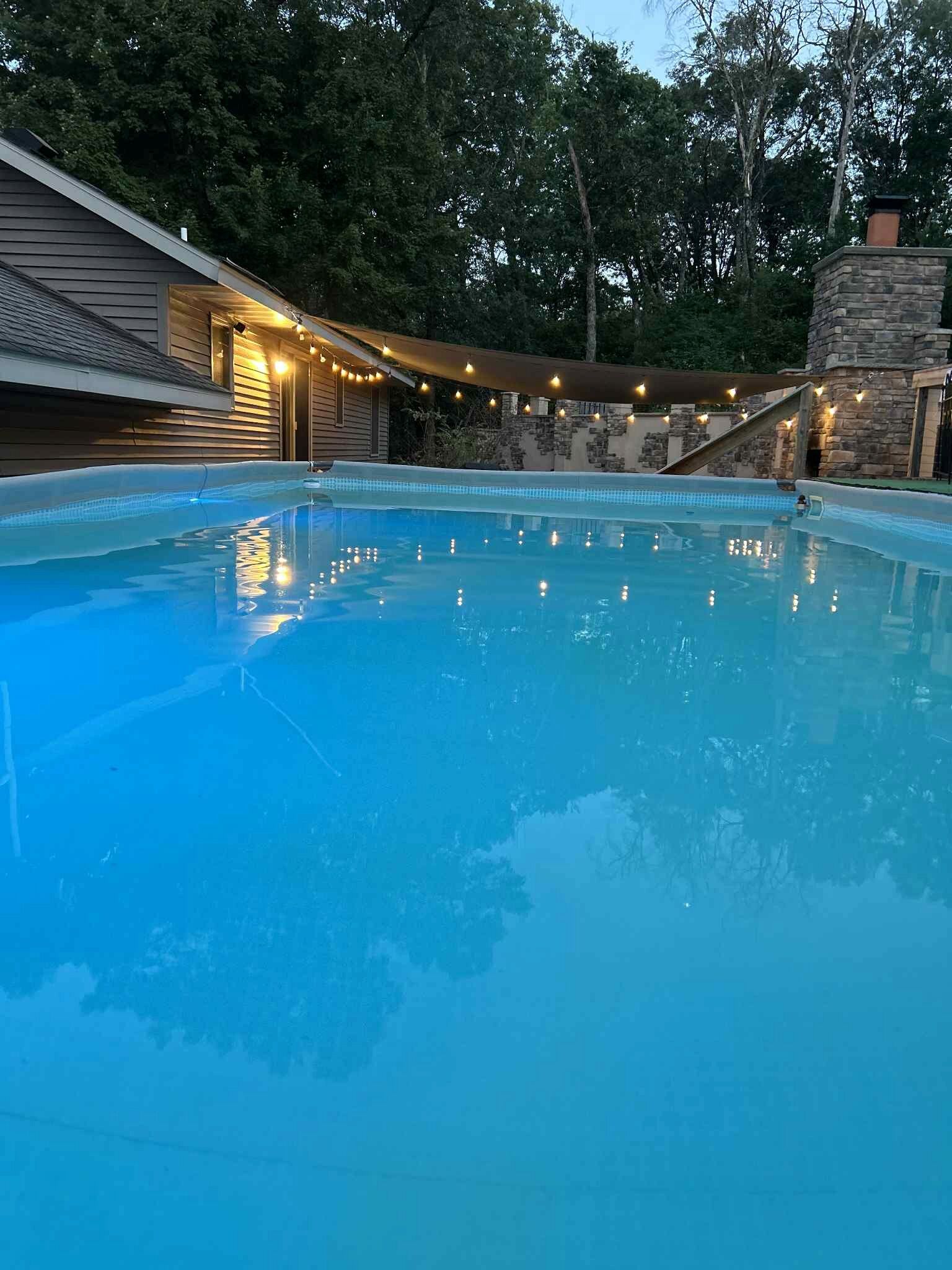 A swimming pool with a stone structure and string lights in the background.