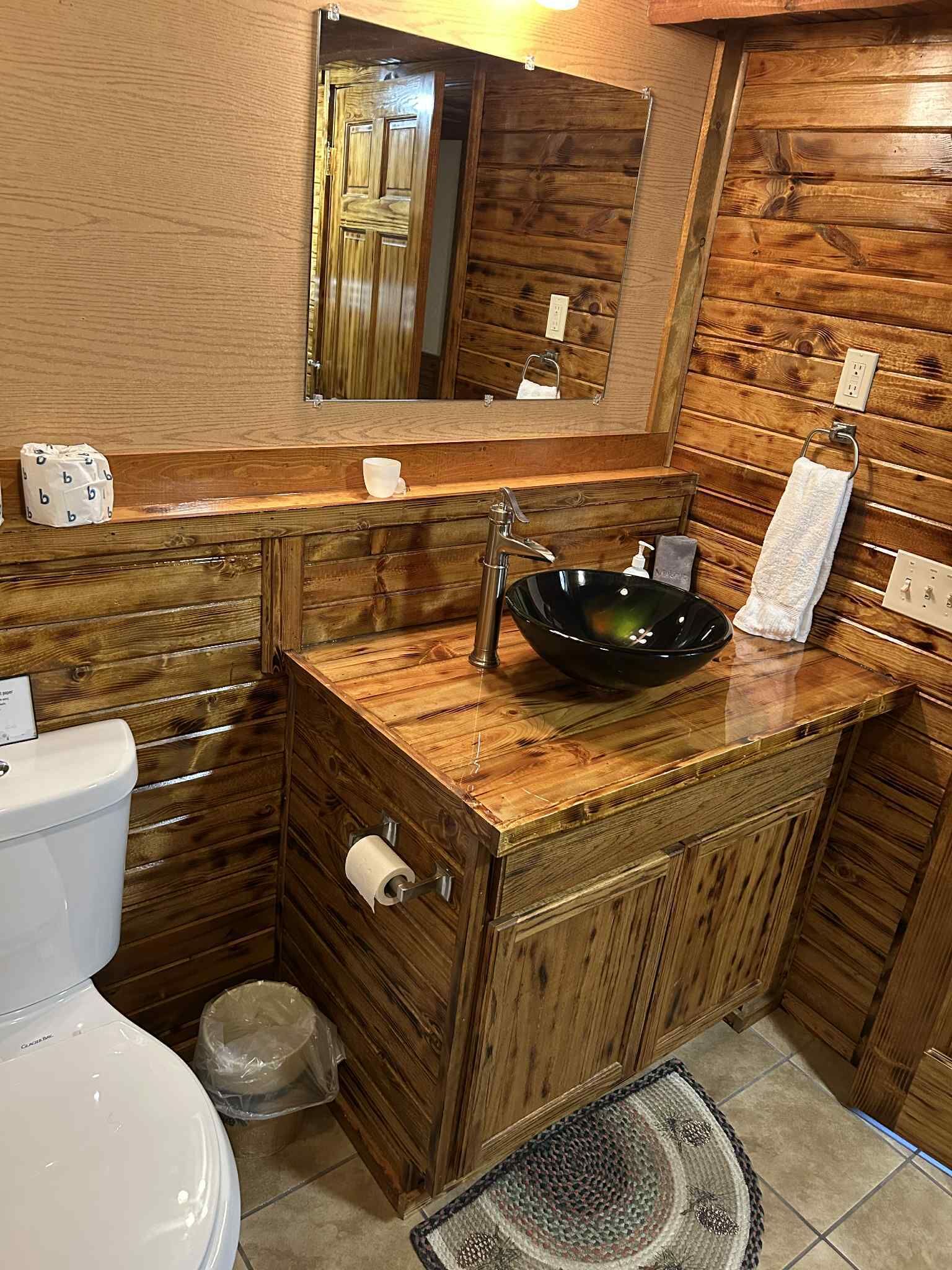 A wooden bathroom with a sink, mirror, and toilet.