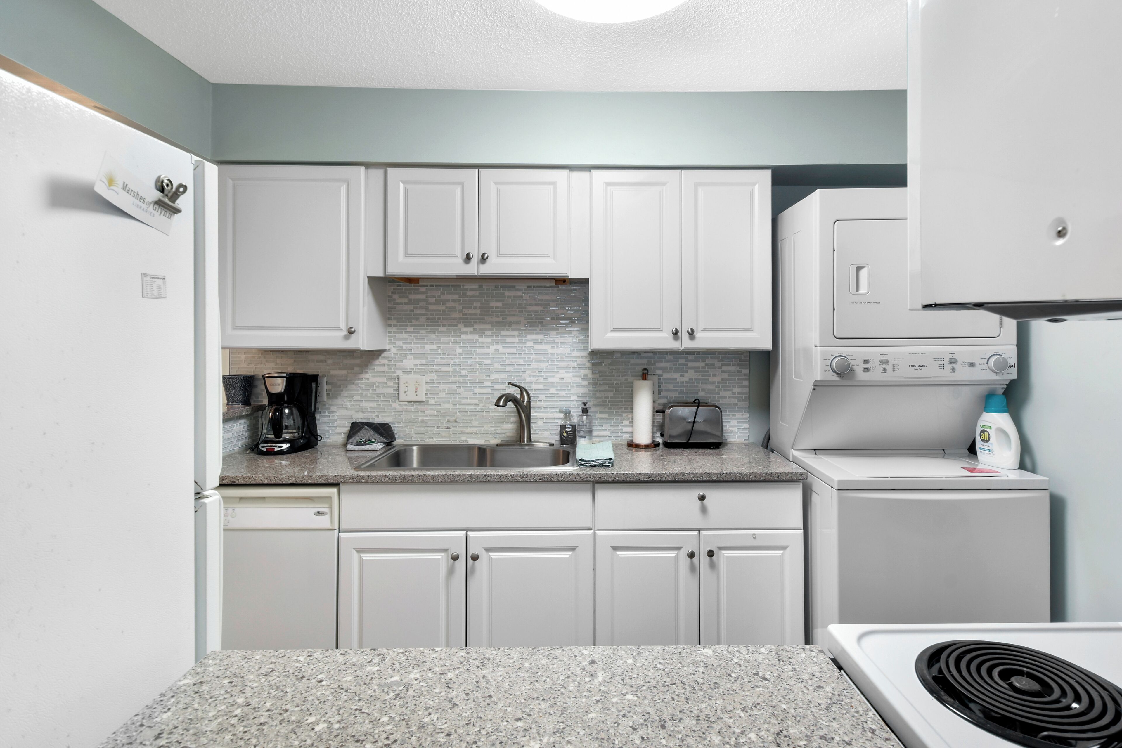 A compact kitchen with white cabinets, a granite countertop, a built-in microwave, and a dishwasher.