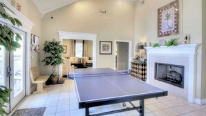 Una sala de estar amplia con una mesa de ping pong, una chimenea y una planta grande.