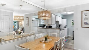 Una cocina moderna con armarios blancos, una mesa de comedor de madera y lámparas colgantes.