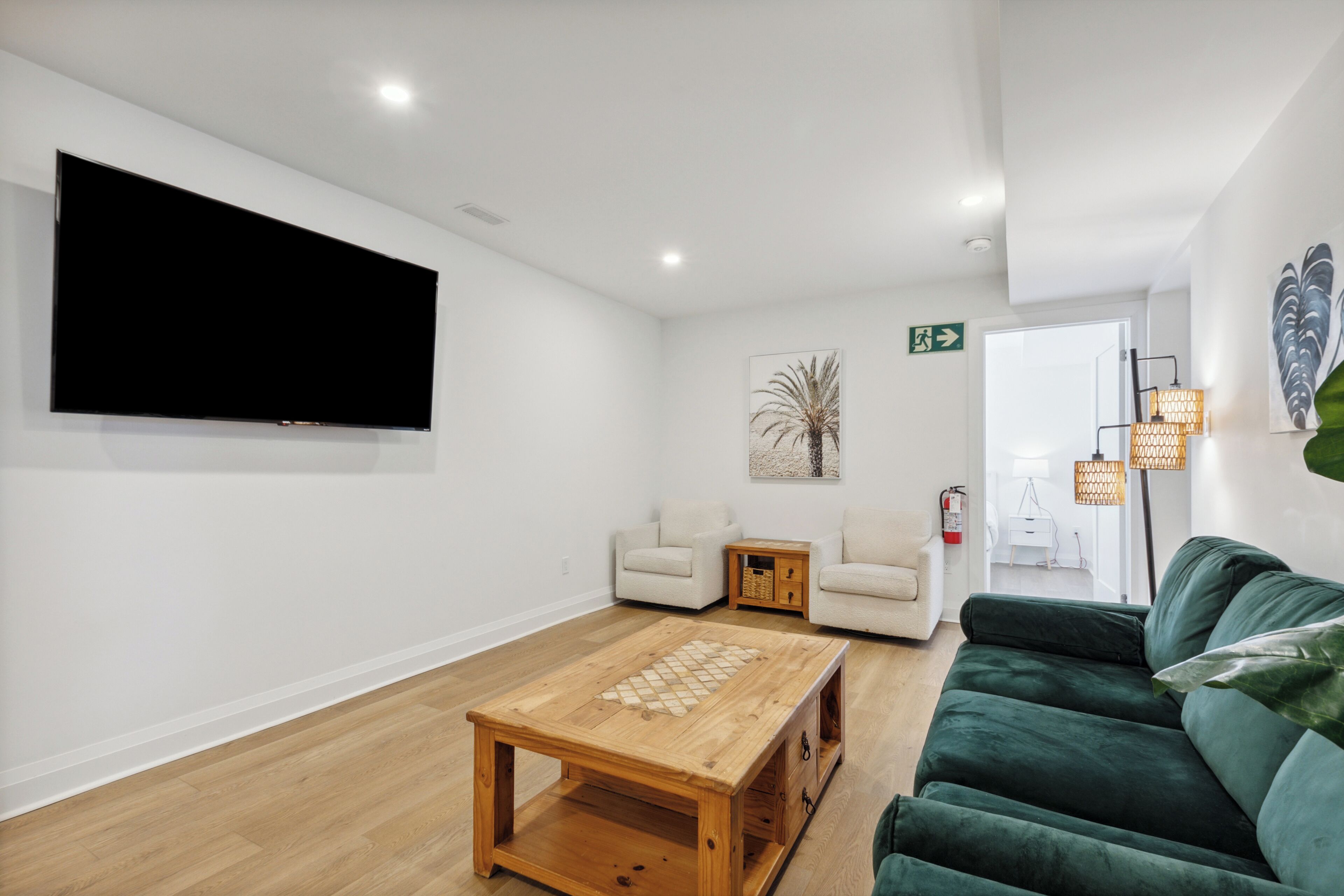 Amplia sala de estar con una gran televisión de pantalla plana, una mesa de centro de madera, un sofá verde y una pequeña mesita auxiliar.