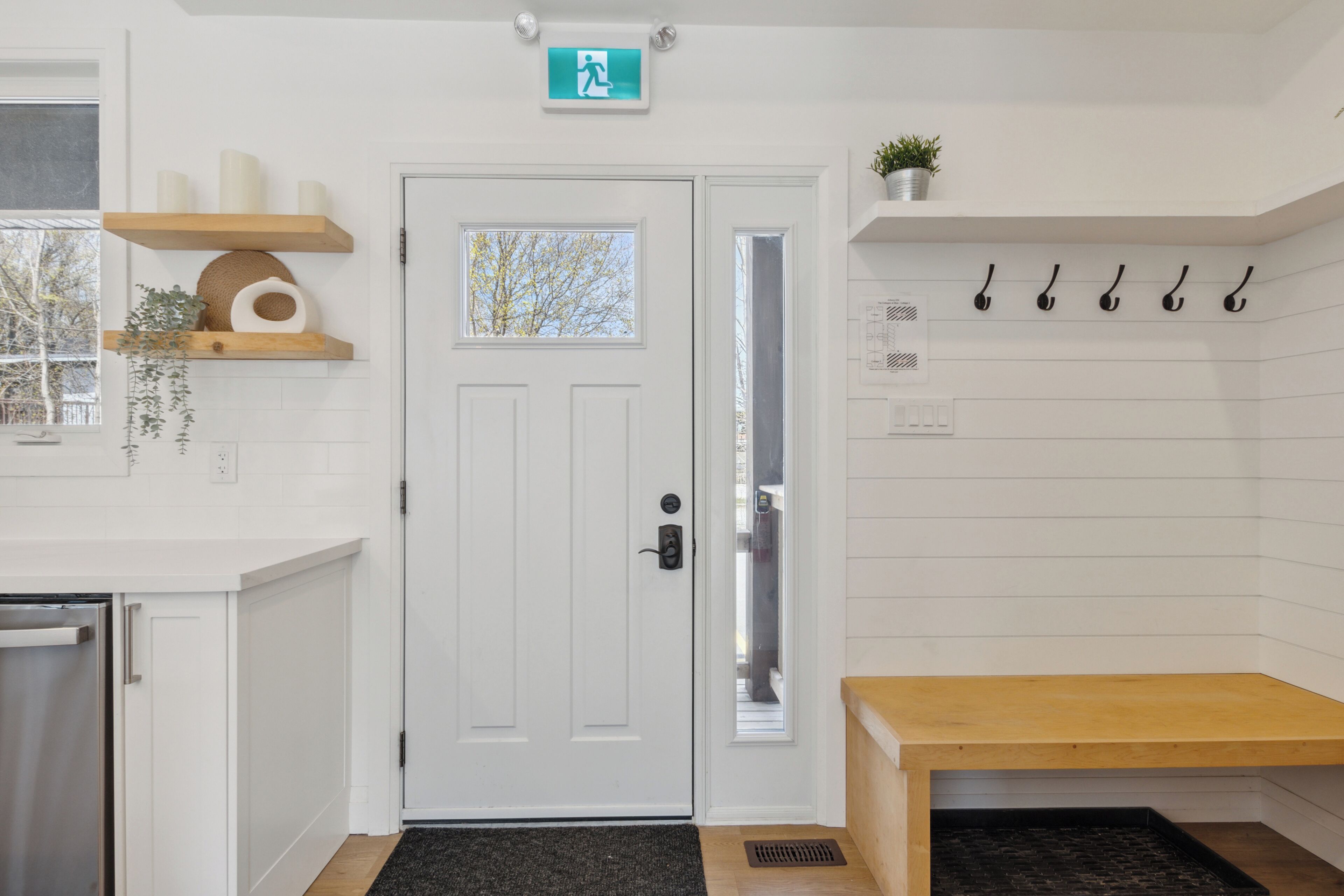 A clean, modern entrance with a white door, a small window, a bench, and a wall-mounted plant.