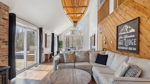 Un interno moderno con soffitto in legno, un divano, un tavolo rotondo e un cartello con su scritto "Blue Mountain Ski Lodge".