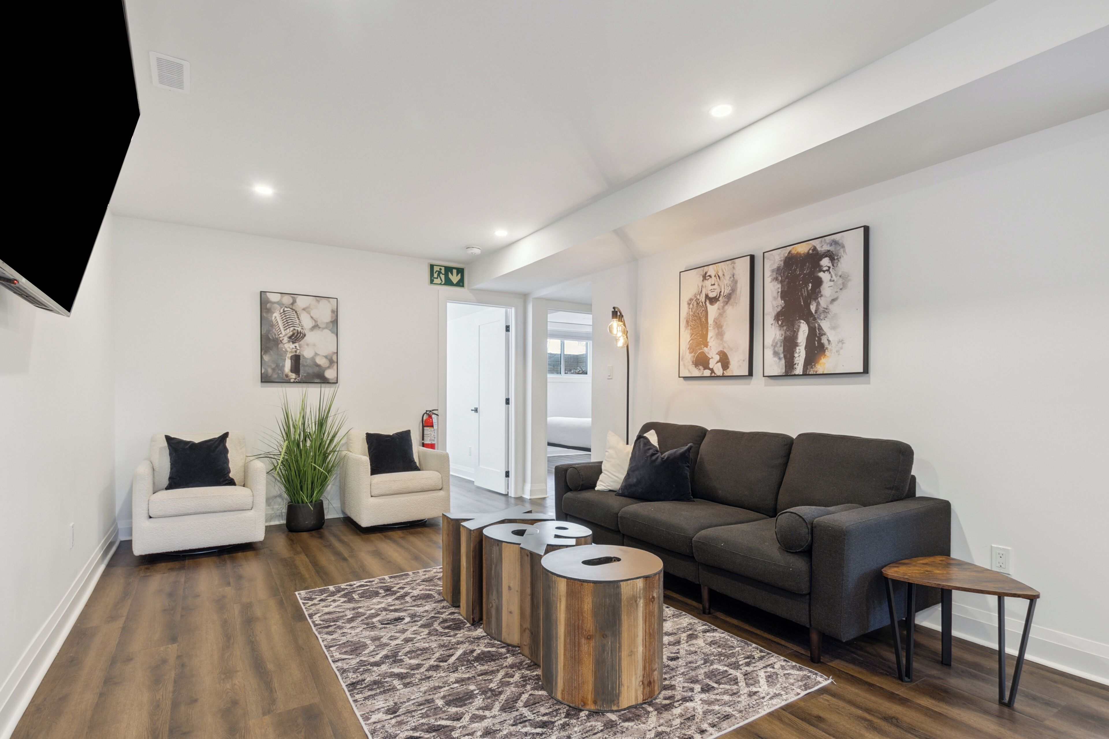 Een moderne woonkamer met een grijze bank, een witte fauteuil en een salontafel. Er hangen twee schilderijen aan de muur en staat een potplant.