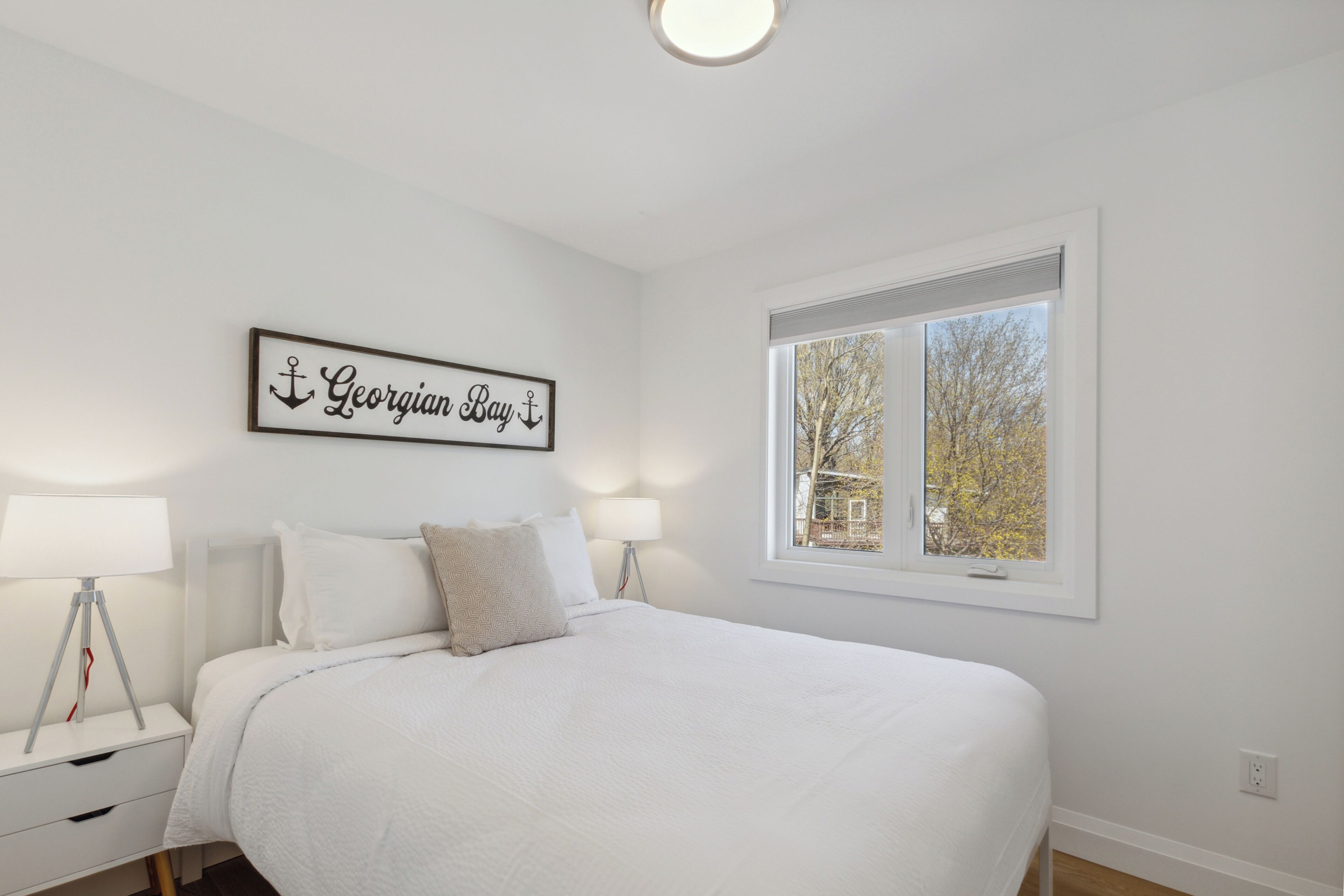 Une chambre à coucher avec un grand lit, deux tables de chevet avec des lampes, une fenêtre donnant sur la forêt et un panneau mural sur lequel on peut lire « Georgiana Bay ».