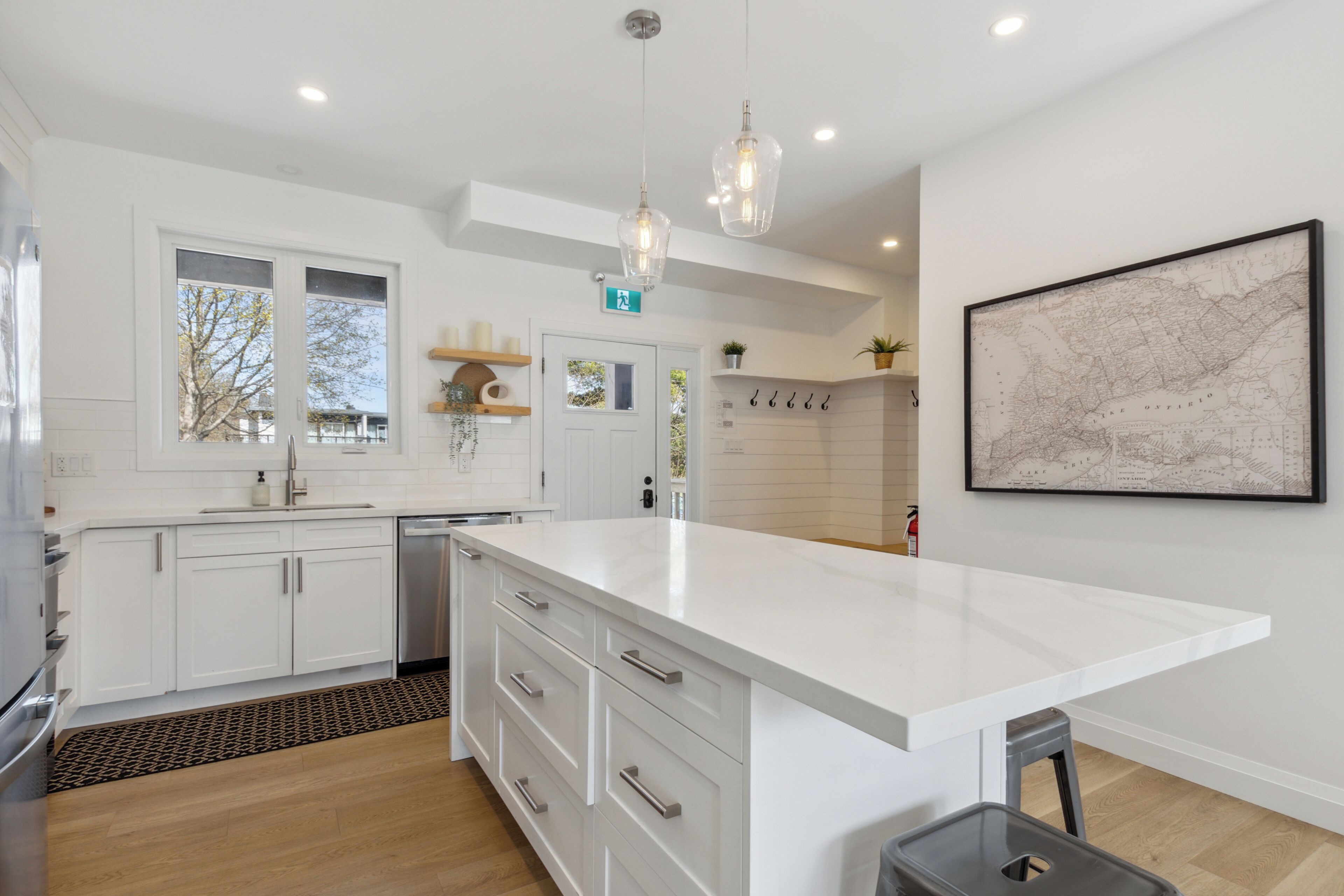 A modern kitchen with white cabinetry, a large island, pendant lighting, and a map on the wall.