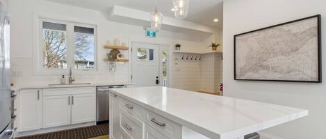 A modern kitchen with white cabinetry, a large island, pendant lighting, and a map on the wall.