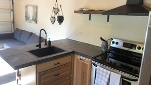 Une cuisine de taille réduite, équipée d’un évier, de meubles de rangement en bois, d’une cuisinière et d’une fenêtre située au-dessus de l’évier.