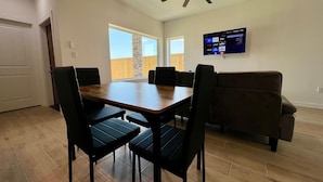 Un comedor con una mesa de madera y sillas negras, un ventilador de techo y un televisor en la pared.